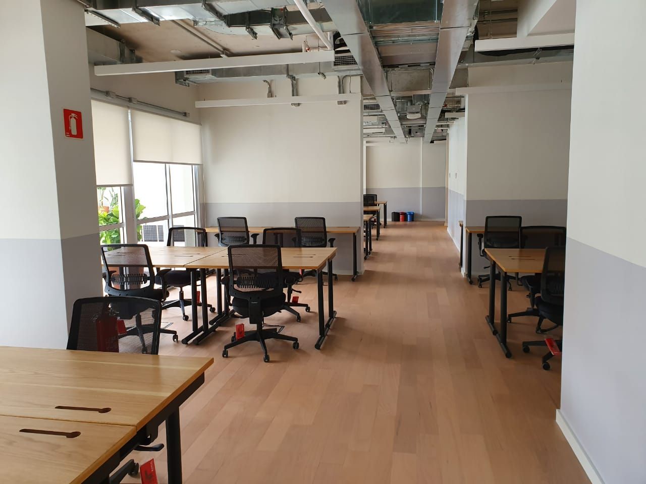 Escritório moderno vazio com mesas, cadeiras e piso de madeira clara em um espaço de trabalho aberto.
