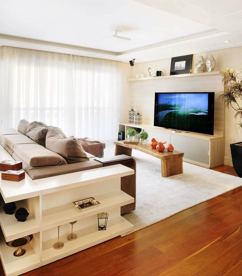 Sala de estar iluminada com sofá seccional bege, TV de parede, lareira, tapete branco e piso de madeira.