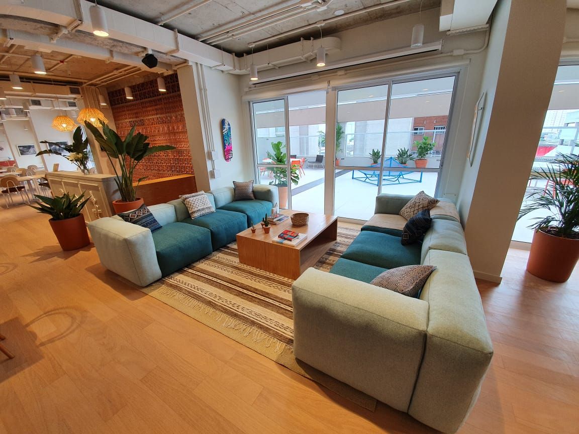 Sala de estar moderna com sofás azul-petróleo, mesa de centro de madeira, plantas em vasos e grandes portas de vidro que dão para um pátio junto à piscina.
