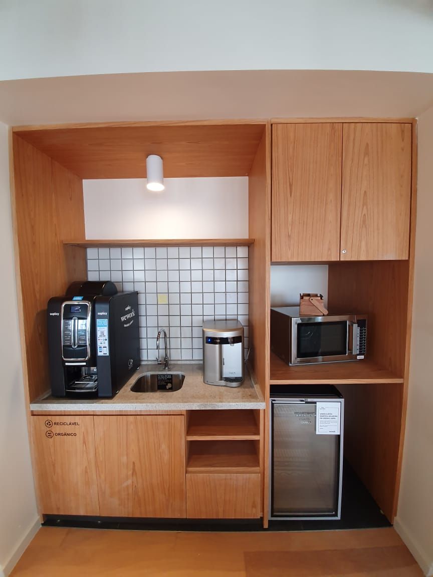 Cozinha compacta embutida com cafeteira, micro-ondas, frigobar e armários em um nicho de madeira.