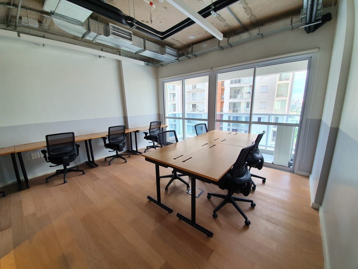Sala de conferências moderna com mesa comprida de madeira, cadeiras pretas e grandes janelas com vista para edifícios de escritórios.