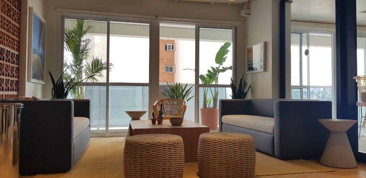 Sala de estar moderna com sofás azuis, bancos de vime e portas de vidro deslizantes com vista para uma varanda.