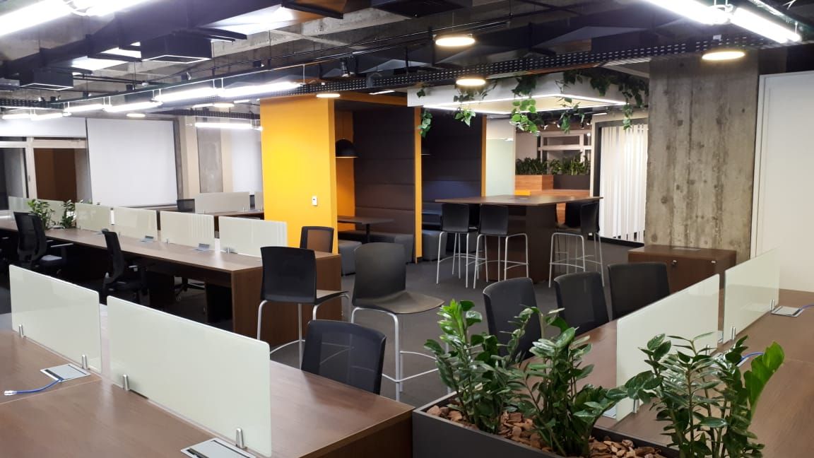 Sala de estar de escritório em plano aberto com mesas, cadeiras pretas, plantas e paredes com detalhes em laranja.