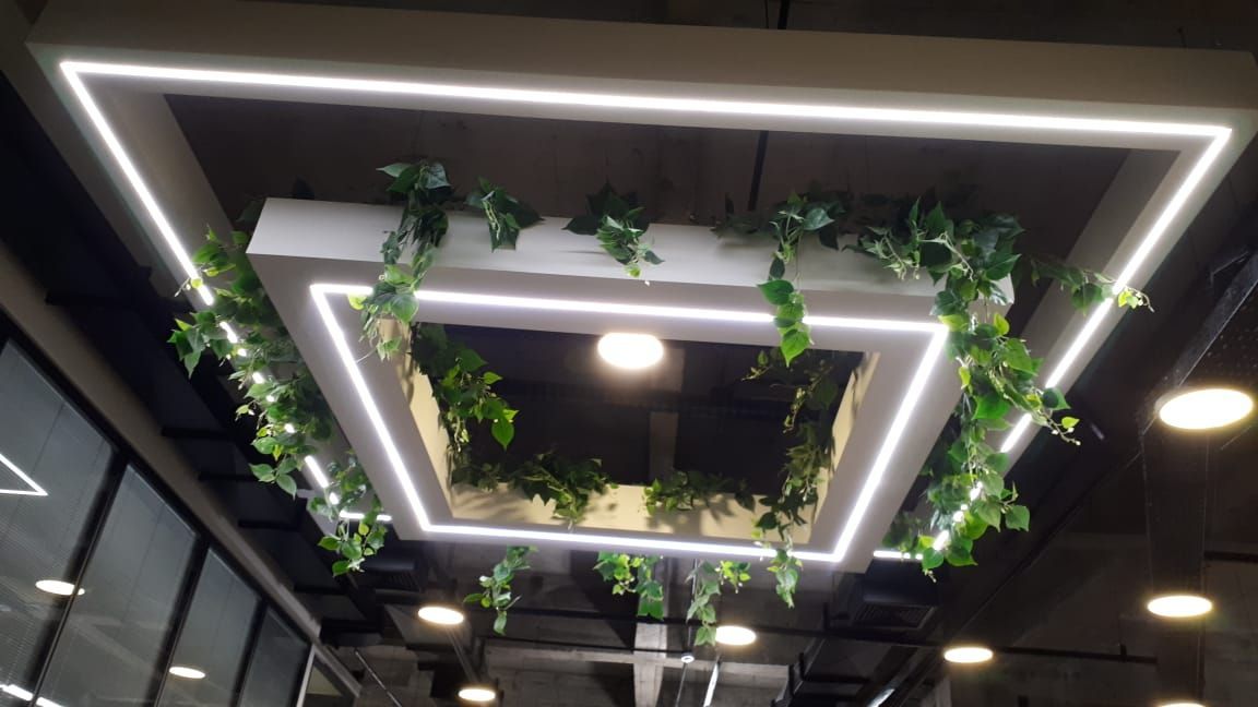 Luminárias de teto geométricas com trepadeiras verdes pendentes em um espaço interno moderno.