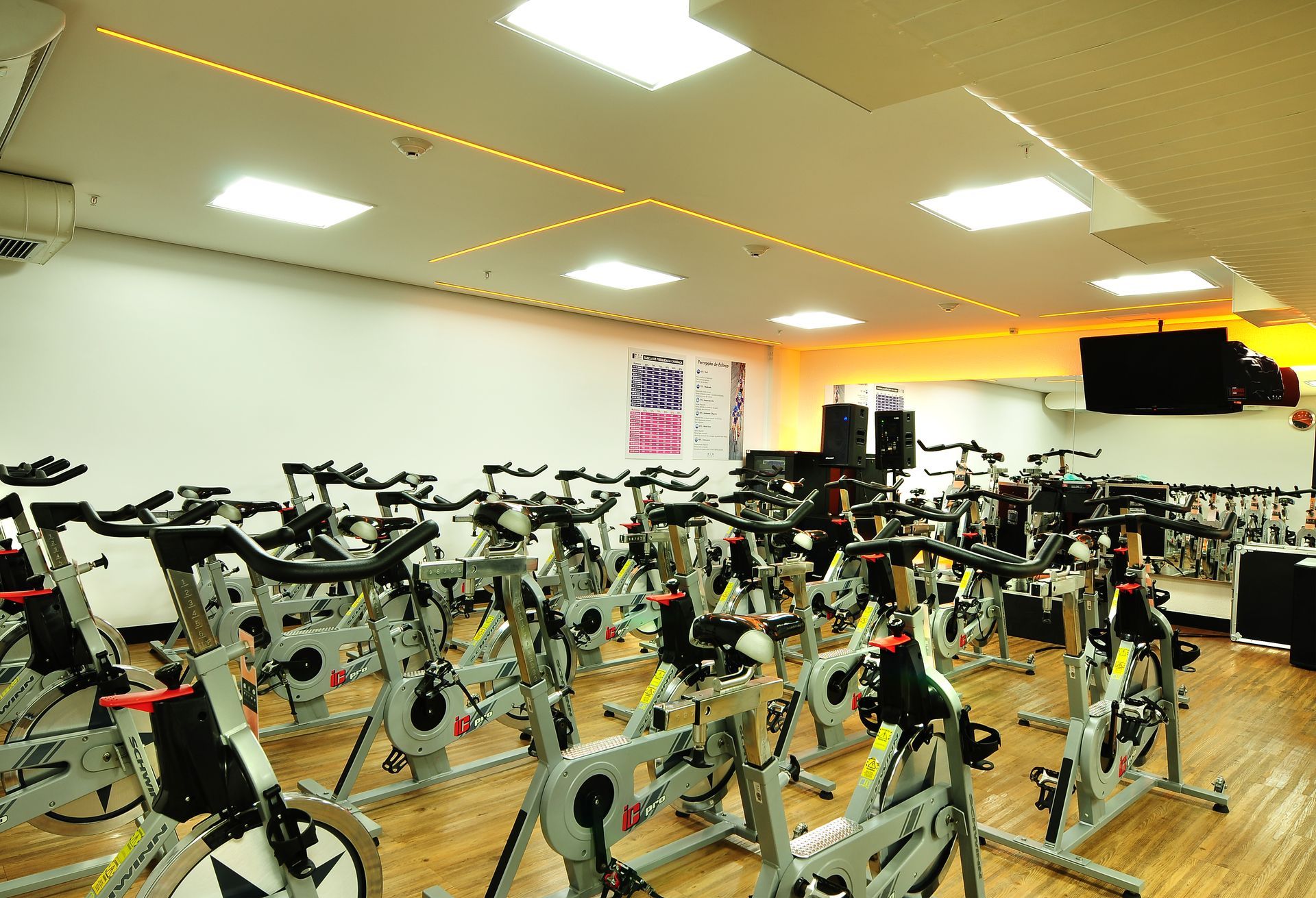 Estúdio de ciclismo indoor com fileiras de bicicletas ergométricas sob luzes brilhantes no teto.