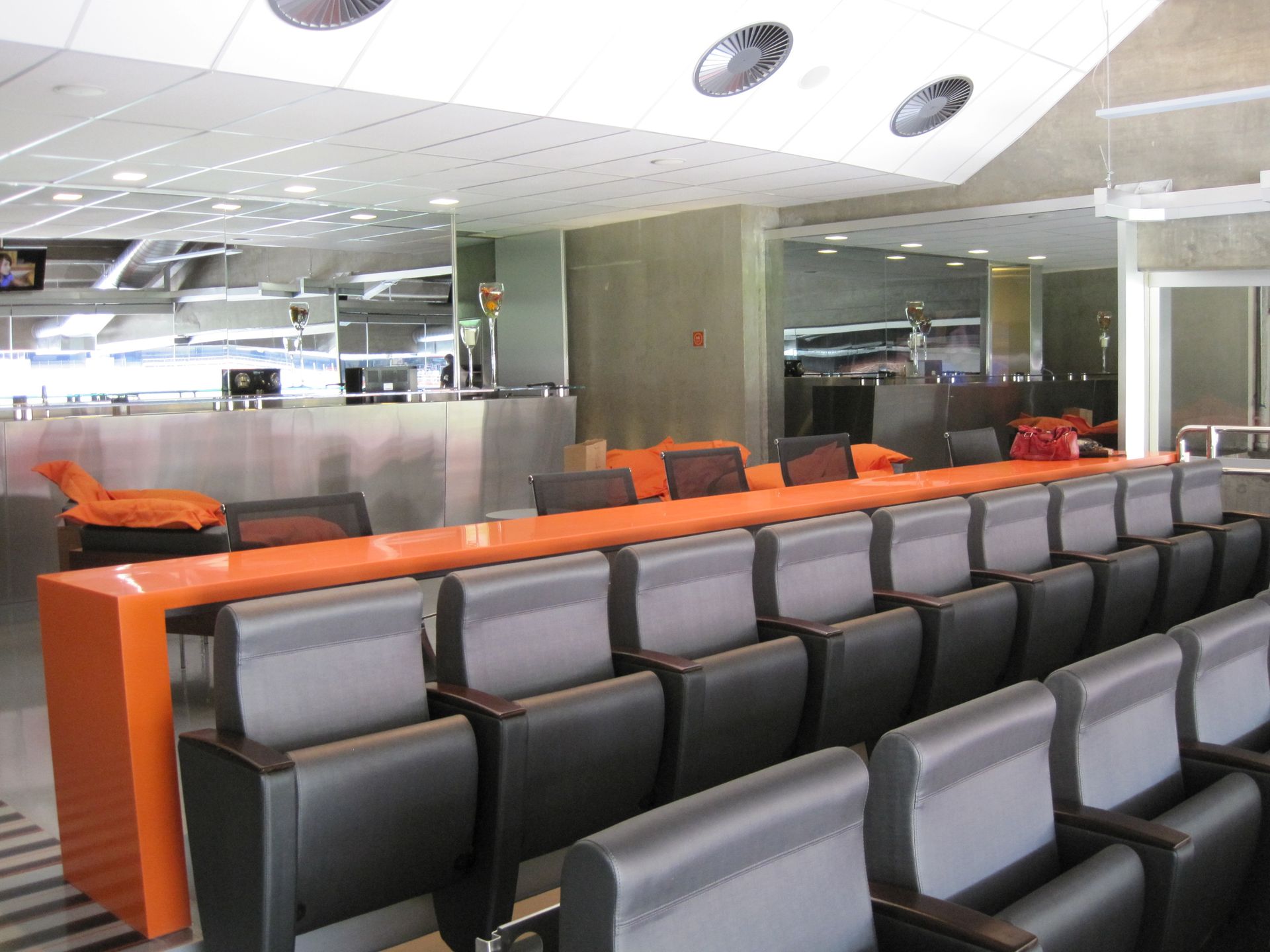 Fileiras de assentos de espera laranja e pretos em um saguão de aeroporto bem iluminado.