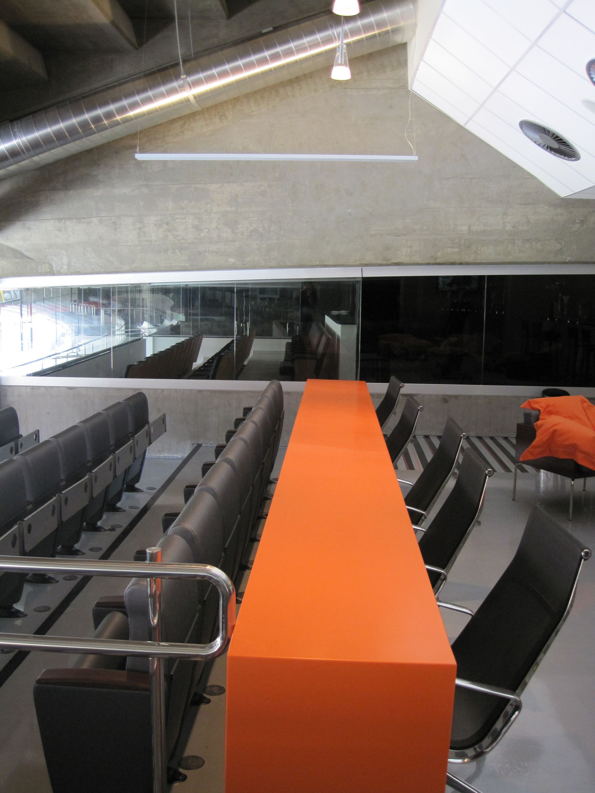 Sala de conferências com fileiras de cadeiras cinzentas e uma mesa laranja brilhante no centro.