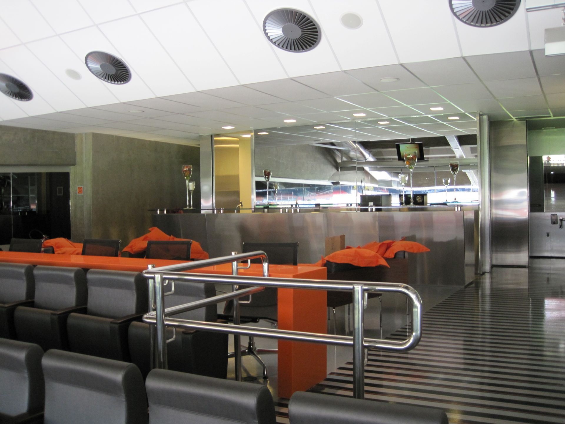 Área de espera vazia de um aeroporto moderno, com assentos laranja e cinza e grades de metal.