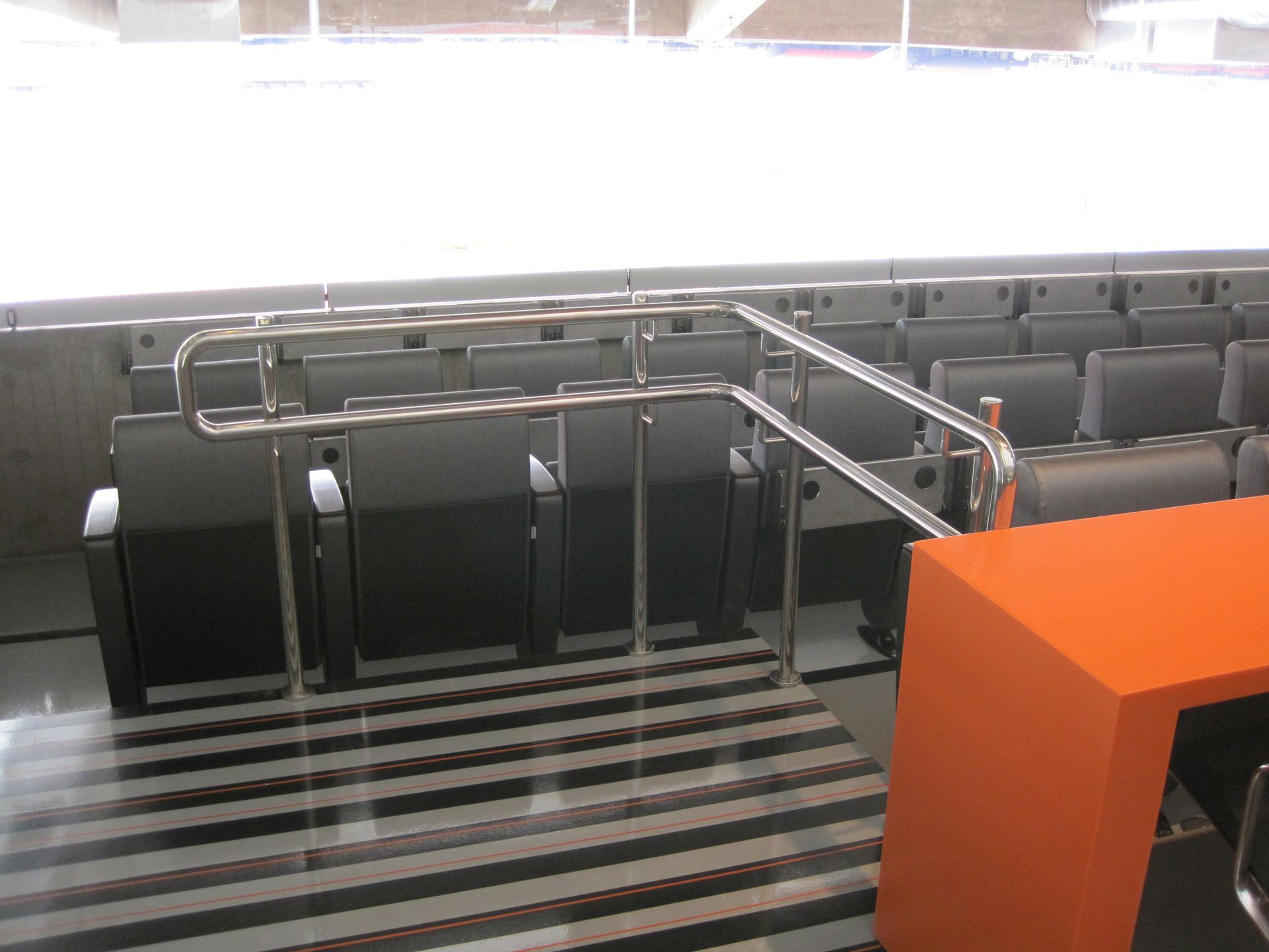 Área de espera vazia do aeroporto com grades de metal e um balcão laranja em primeiro plano.
