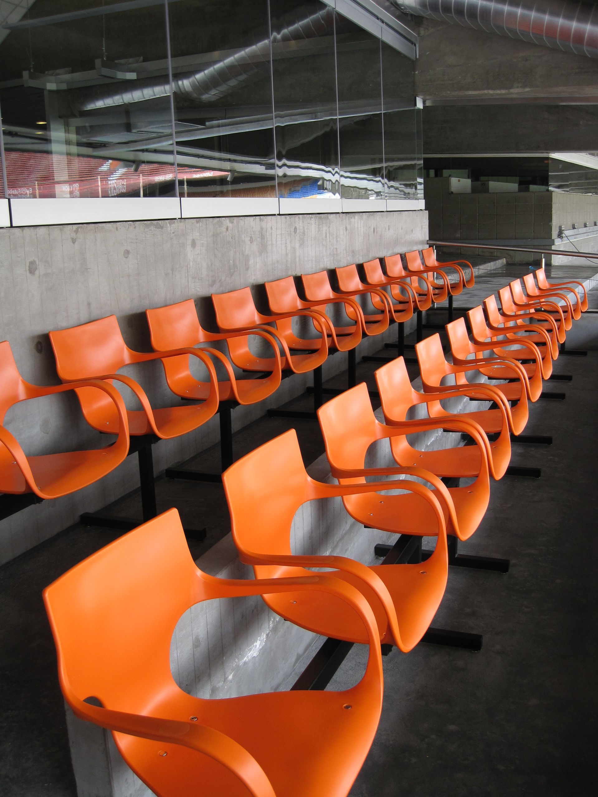 Fileiras de assentos vazios, na cor laranja, em uma arena esportiva coberta.
