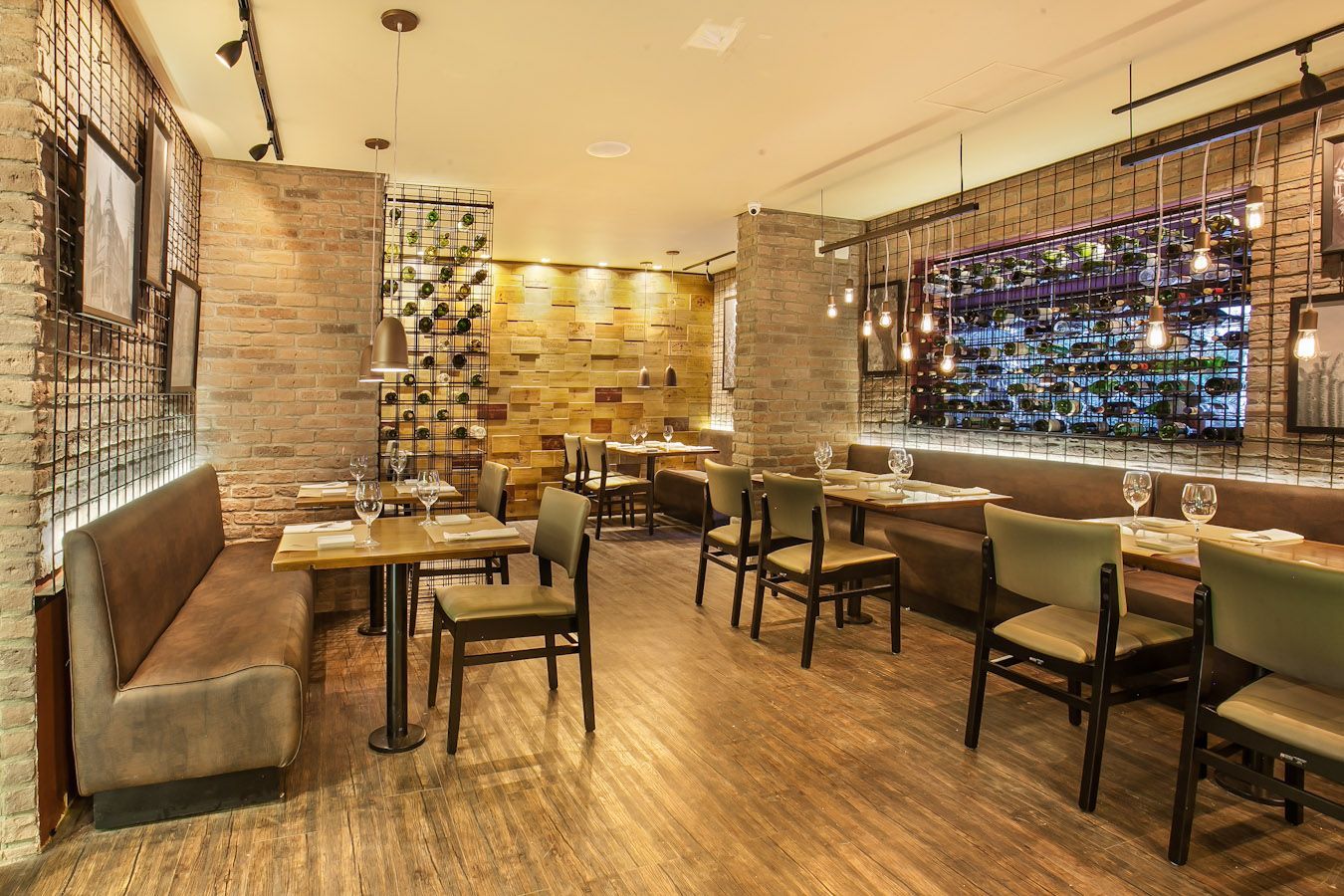 Interior de restaurante moderno e aconchegante com piso de madeira, paredes de tijolos, mesas, cadeiras e iluminação ambiente acolhedora.