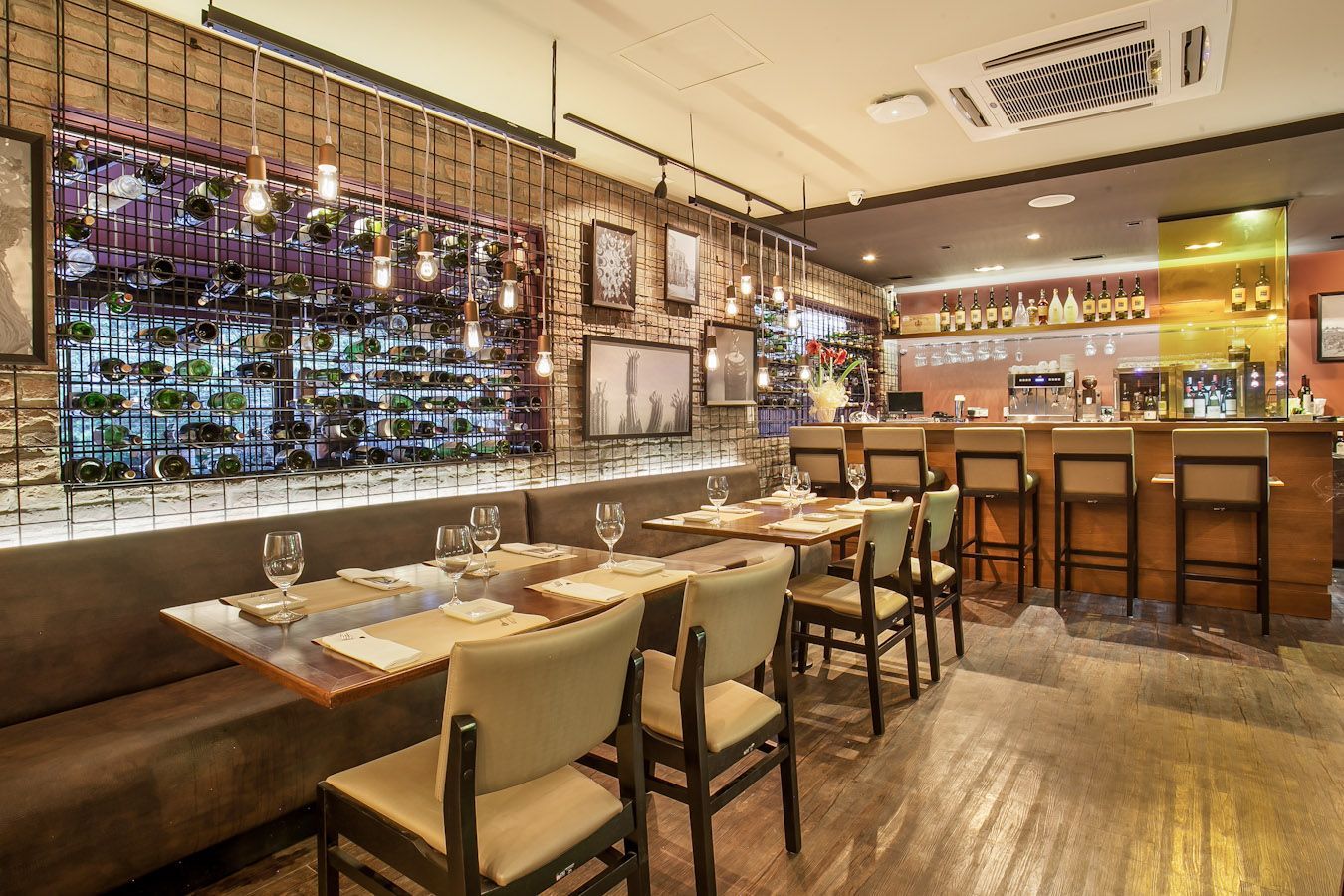 Interior aconchegante de restaurante com mesas postas, balcão de bar, iluminação acolhedora e uma parede decorativa de vinhos.