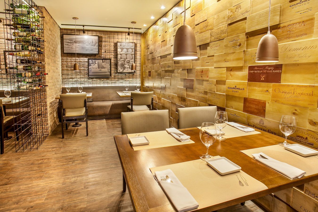 Área de jantar aconchegante do restaurante com mesas de madeira, cadeiras bege, paredes de tijolos e iluminação pendente em tons quentes.