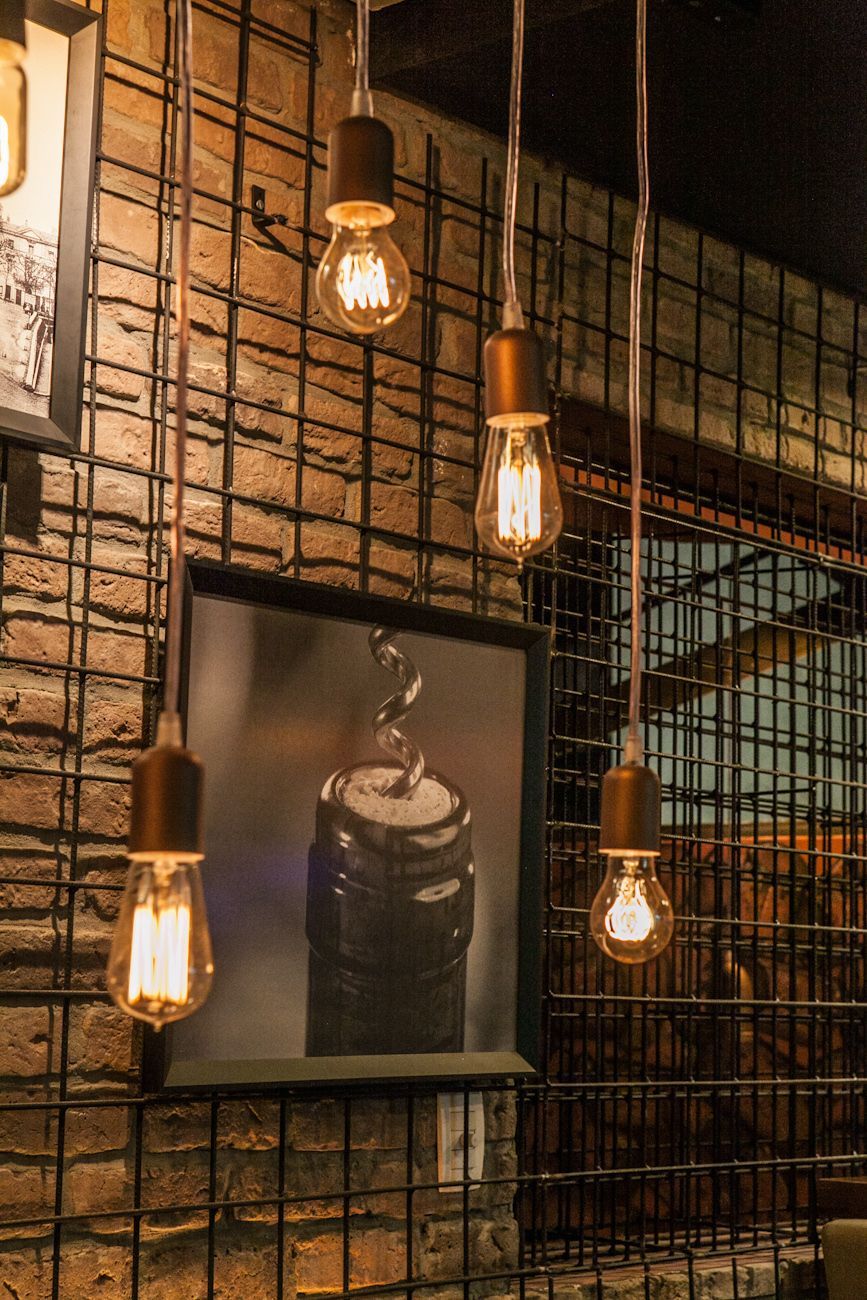 Parede industrial aconchegante com lâmpadas Edison penduradas e uma foto emoldurada em preto e branco sobre tela de arame.