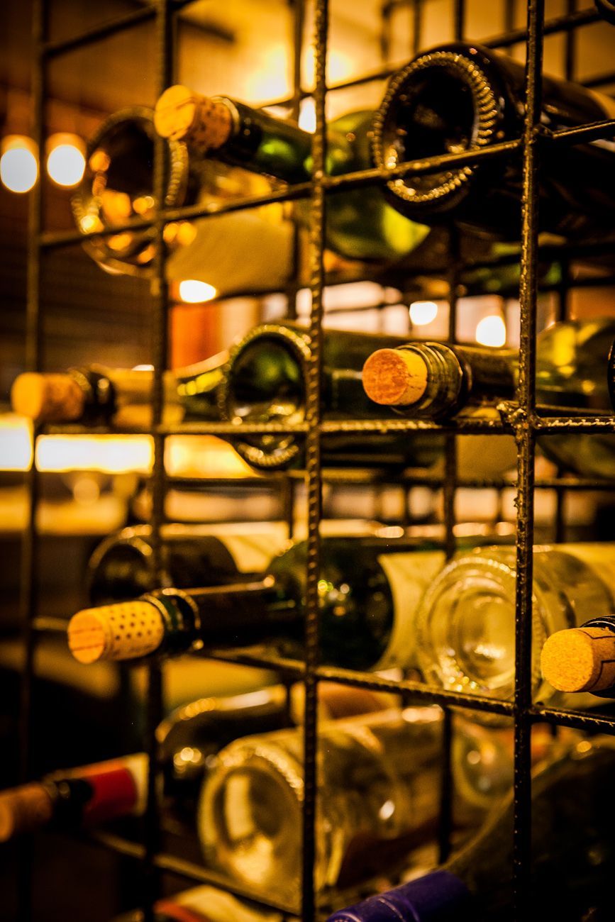 Garrafas de vinho armazenadas em uma prateleira de metal em uma adega com iluminação aconchegante.