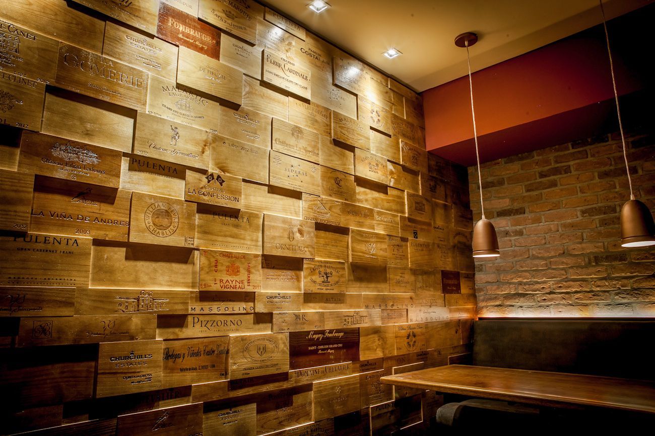 Bar com iluminação aconchegante, paredes de tijolos e madeira, parede texturizada e luminárias pendentes.