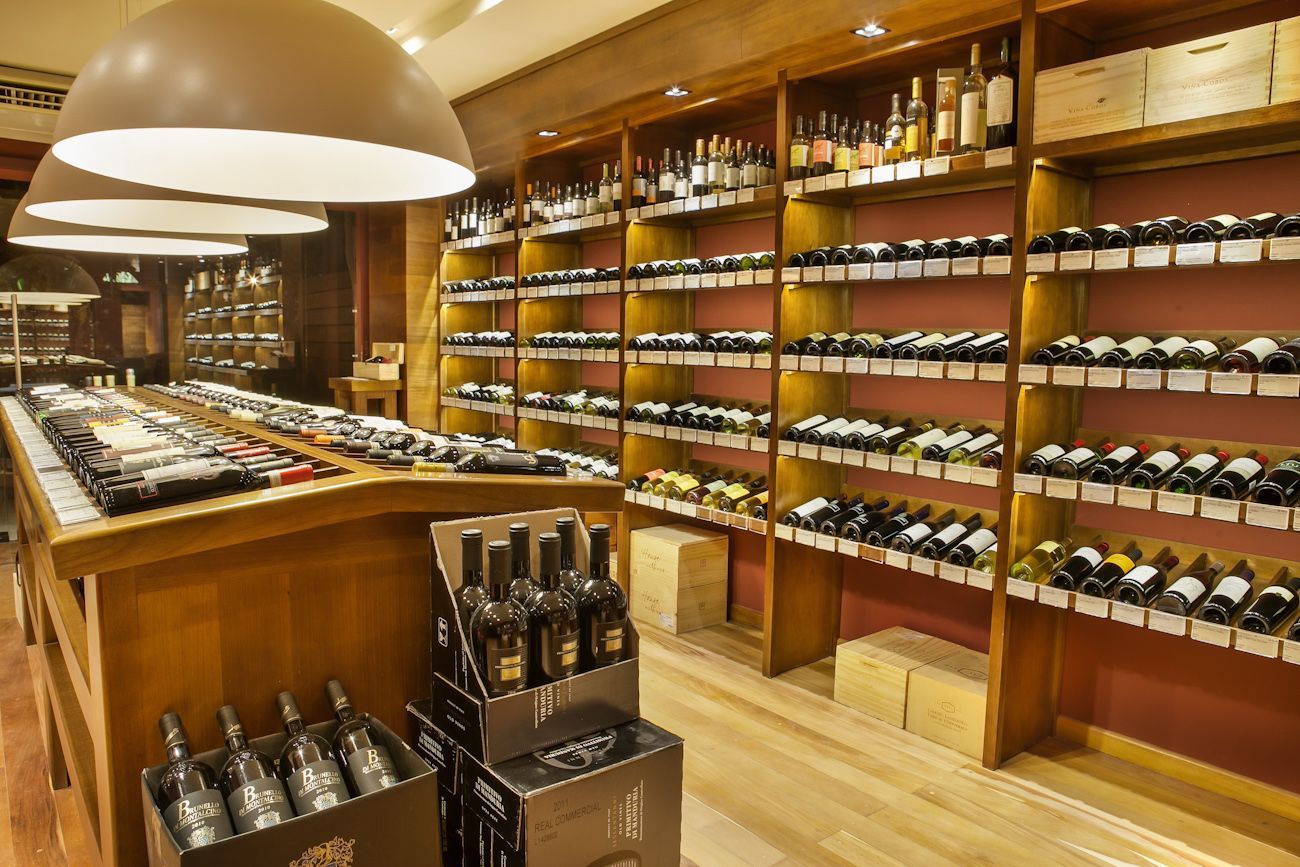Interior de uma loja de vinhos com prateleiras de madeira repletas de garrafas e uma mesa de exposição central sob iluminação aconchegante.