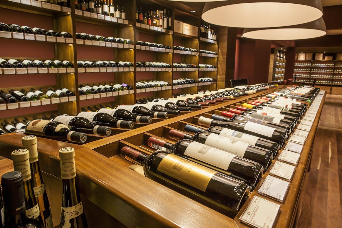 Garrafas de vinho expostas em prateleiras de madeira e uma longa mesa de degustação em uma adega.