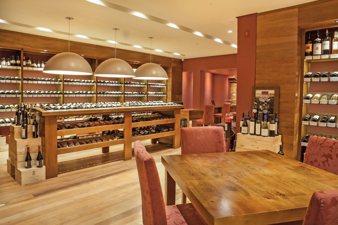 Interior elegante de uma loja de vinhos com mesas de madeira, prateleiras de garrafas e iluminação aconchegante.
