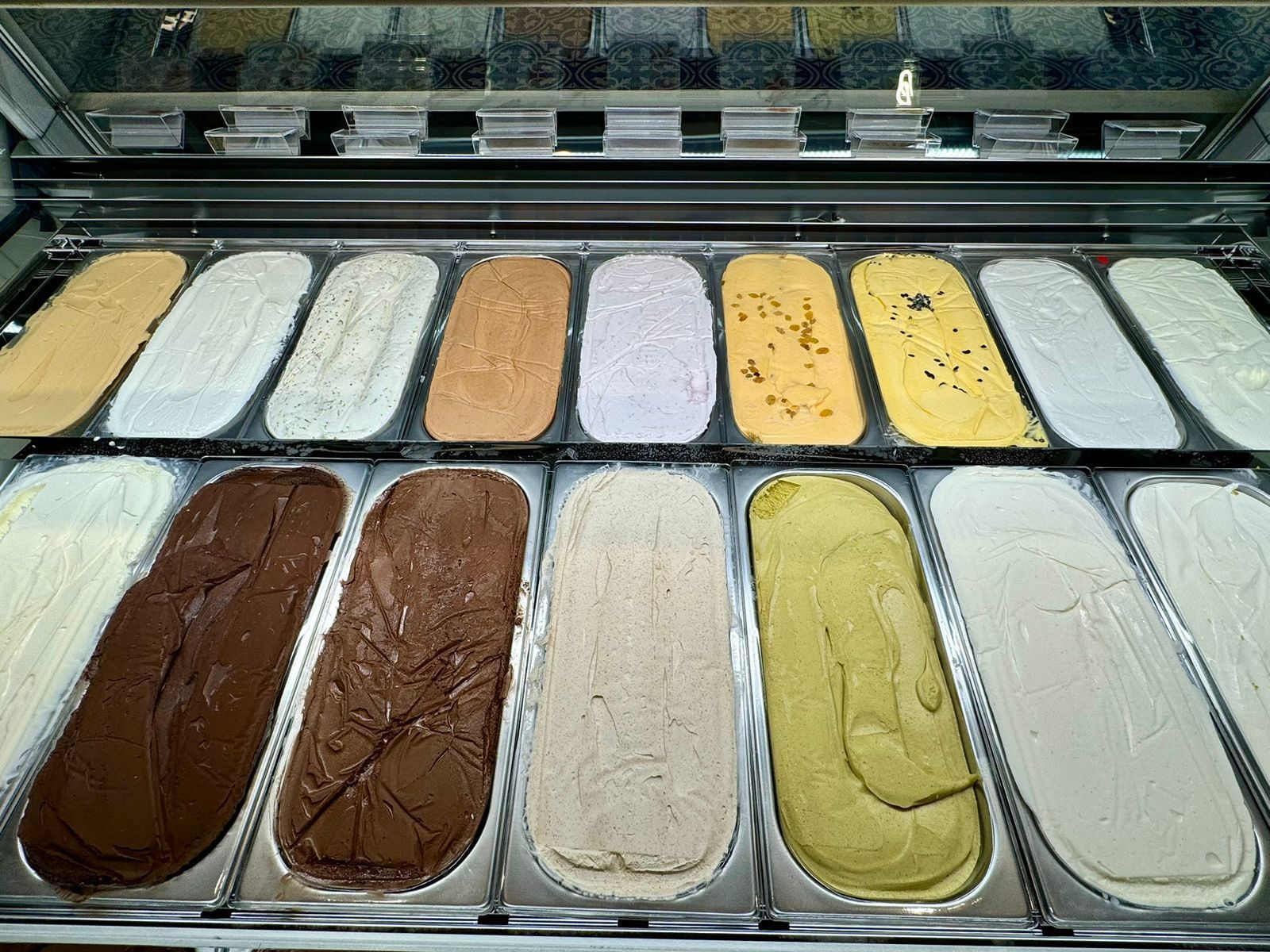 Potes de gelato sortidos em uma vitrine, com sabores branco, marrom, amarelo e bege.