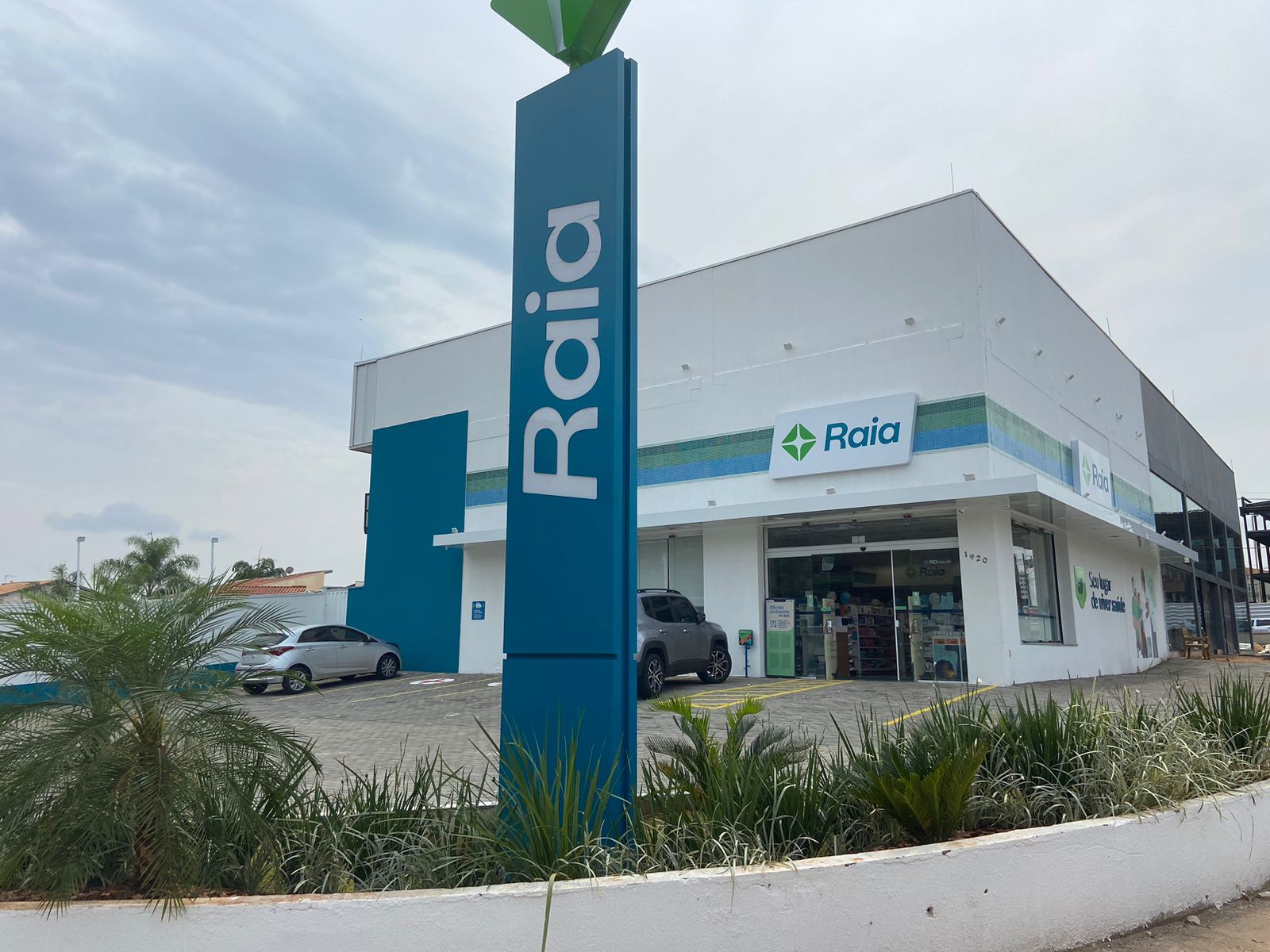 Fachada da farmácia Raia com placa azul e exterior do prédio branco.