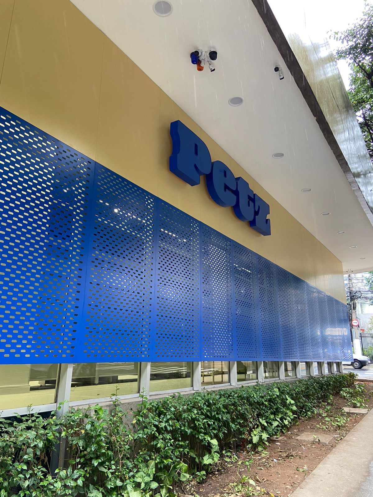 Vista externa de uma placa azul de um banco em um prédio bege com uma cerca viva ao longo da base.