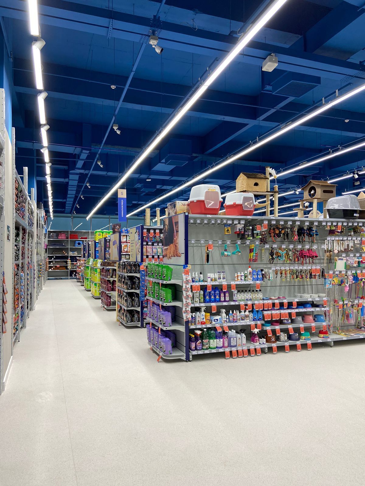 Corredor de uma loja com prateleiras de produtos coloridos sob luzes azuis brilhantes no teto.