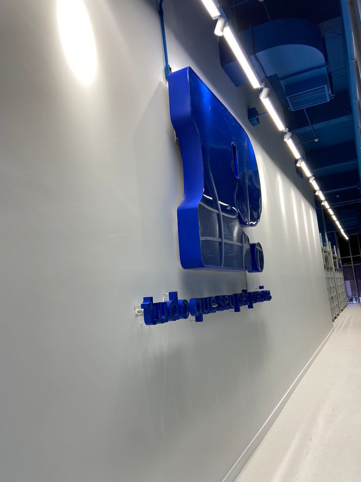 Logotipo azul em uma parede branca em um corredor moderno com luzes de teto e piso polido.