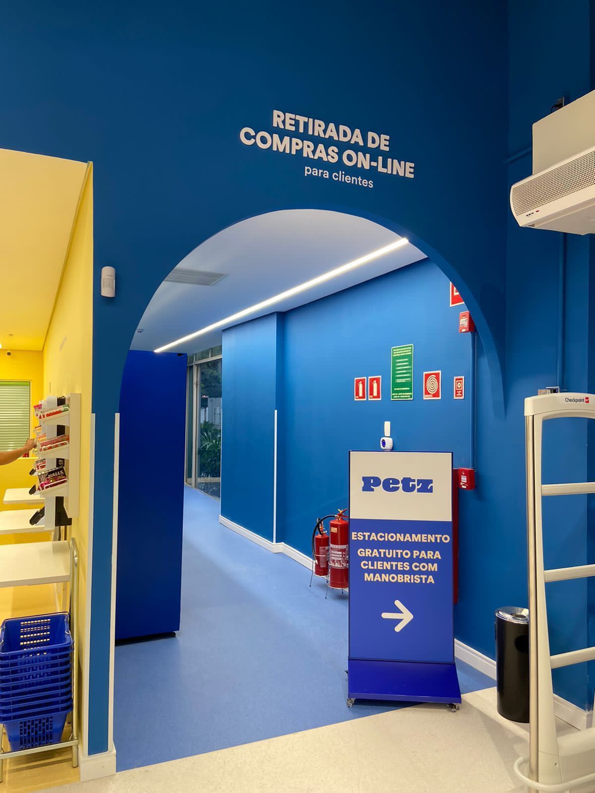 Entrada para retirada de compras na loja com arco azul e placa com os dizeres “Retirada de compras on-line”