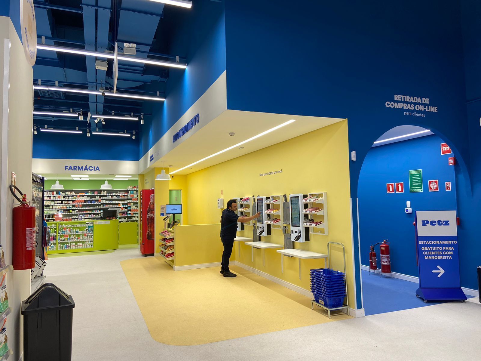 Interior de loja em tons vibrantes de azul e amarelo, com prateleiras, cartazes e uma pessoa olhando os produtos no balcão.
