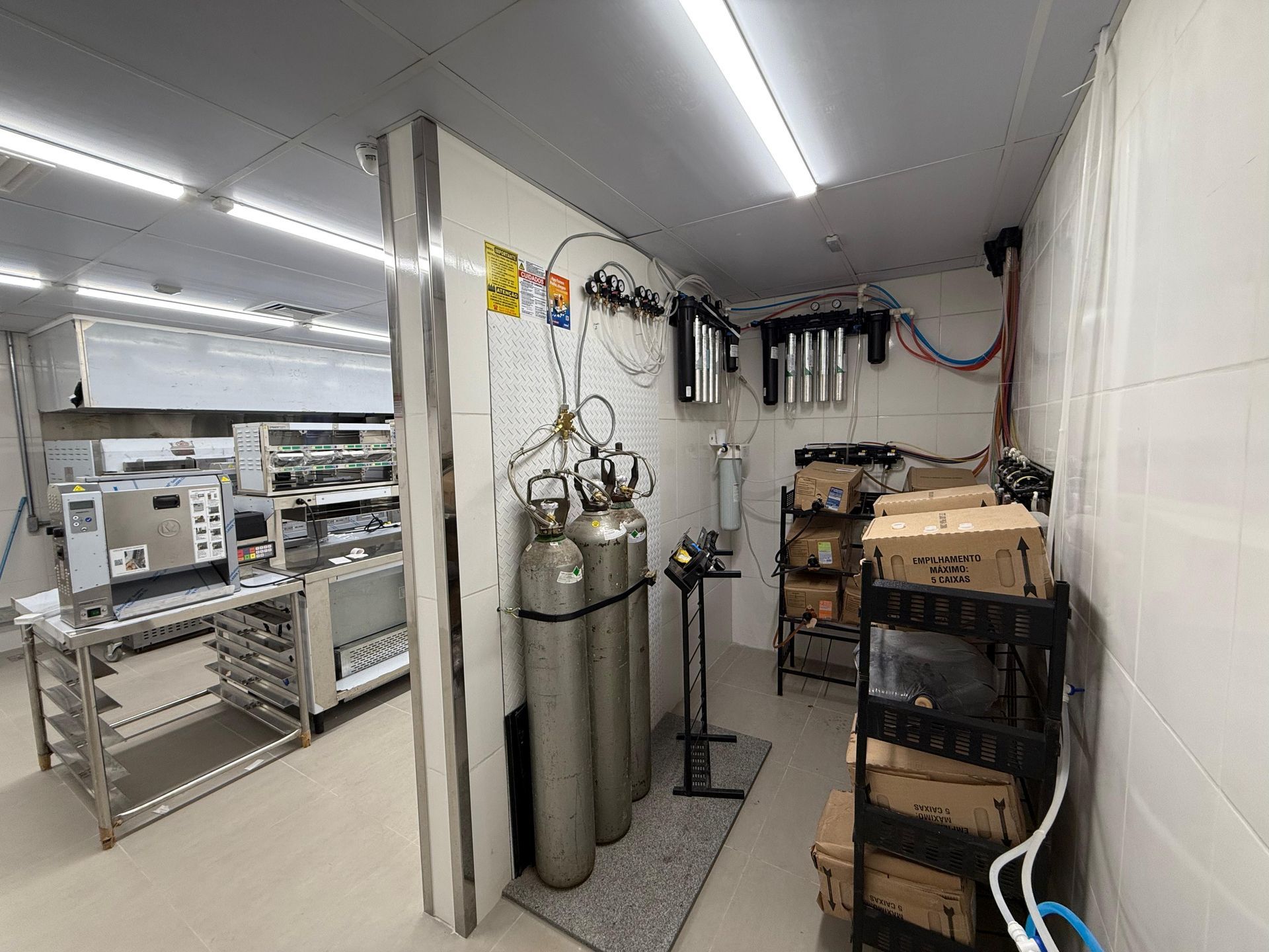 Sala de armazenamento industrial com cilindros de gás, prateleiras e caixas empilhadas ao longo de um corredor estreito.