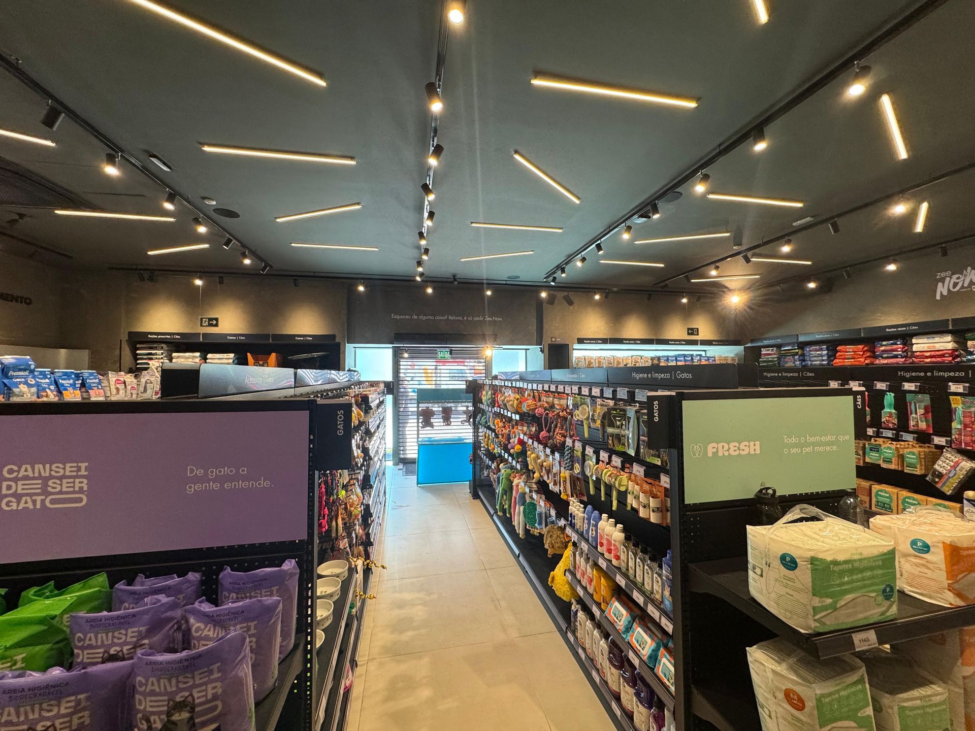 Corredor de supermercado bem iluminado, com prateleiras de lanches e uma passagem central sob luzes de teto.