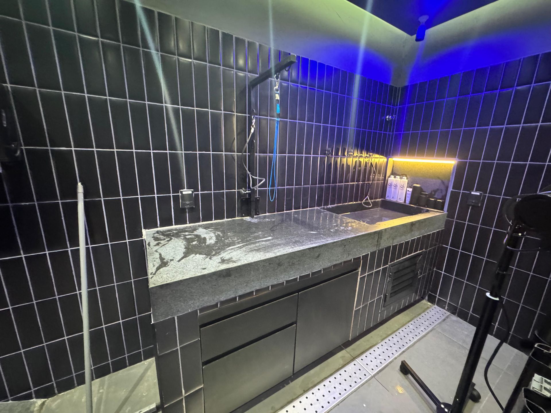 Cozinha moderna com paredes revestidas de azulejos pretos, bancada de pedra e iluminação LED azul sob os armários.