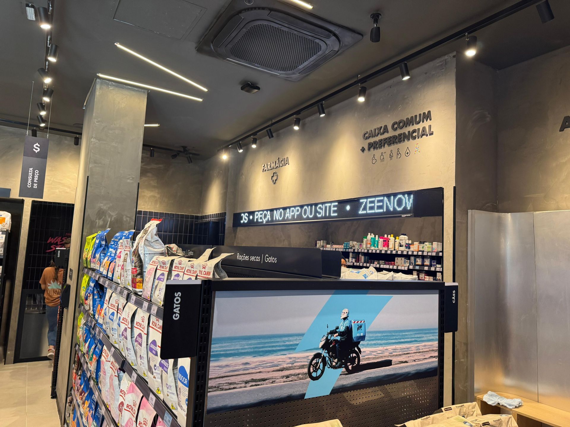 Interior da loja com prateleiras de produtos embalados e um balcão exibindo um pôster de motocicleta.