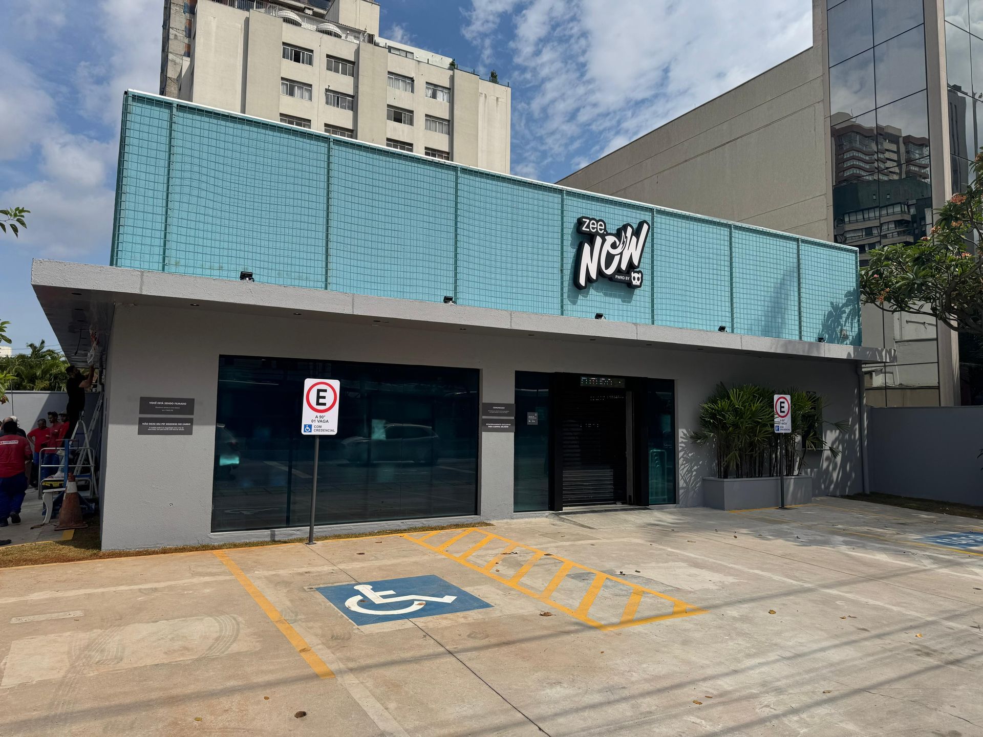 Loja com toldo azul, vagas de estacionamento e vagas acessíveis para cadeirantes em frente a um prédio.