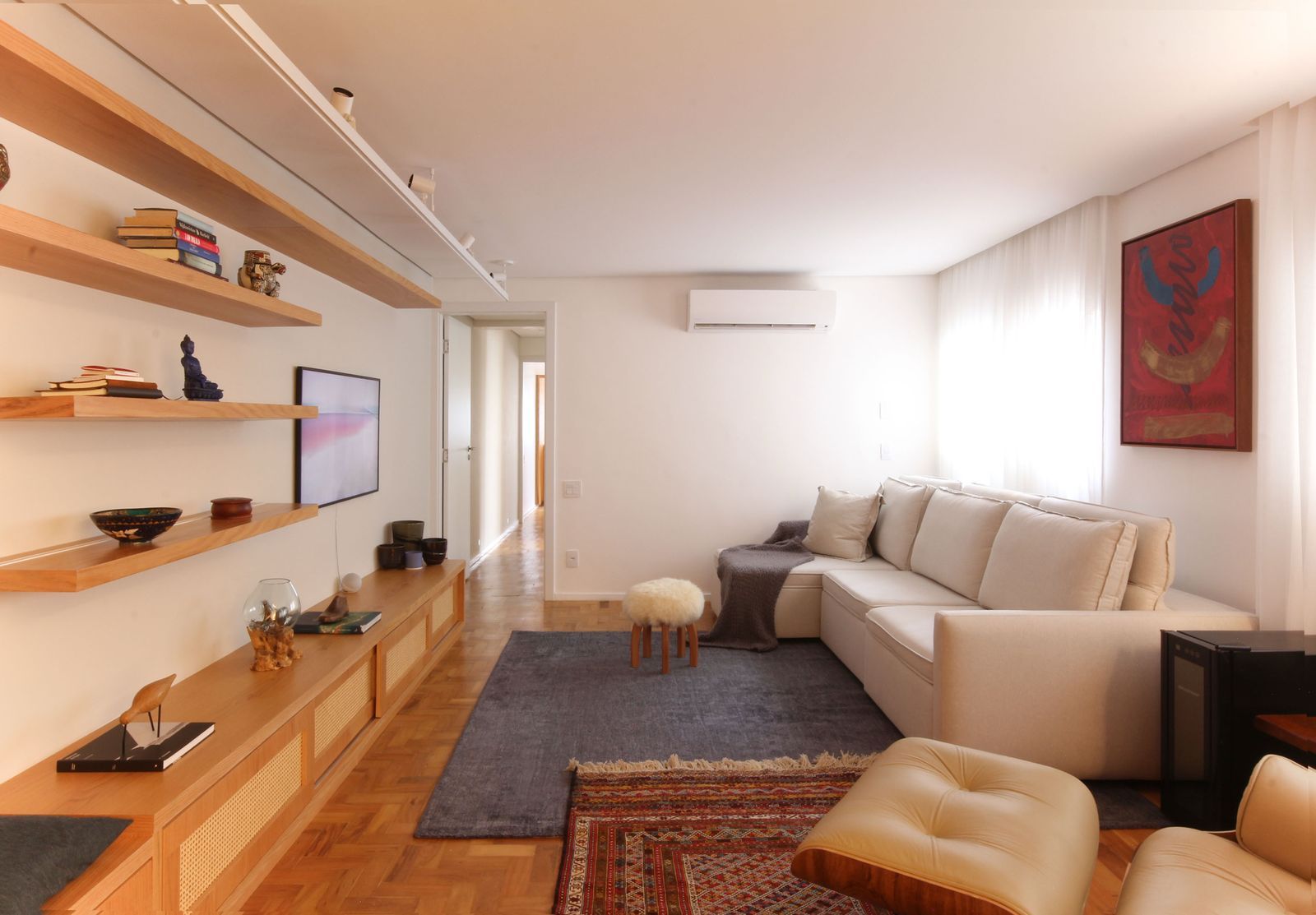 Sala de estar moderna com sofá modular bege, prateleiras flutuantes, TV e arte de parede vermelha.