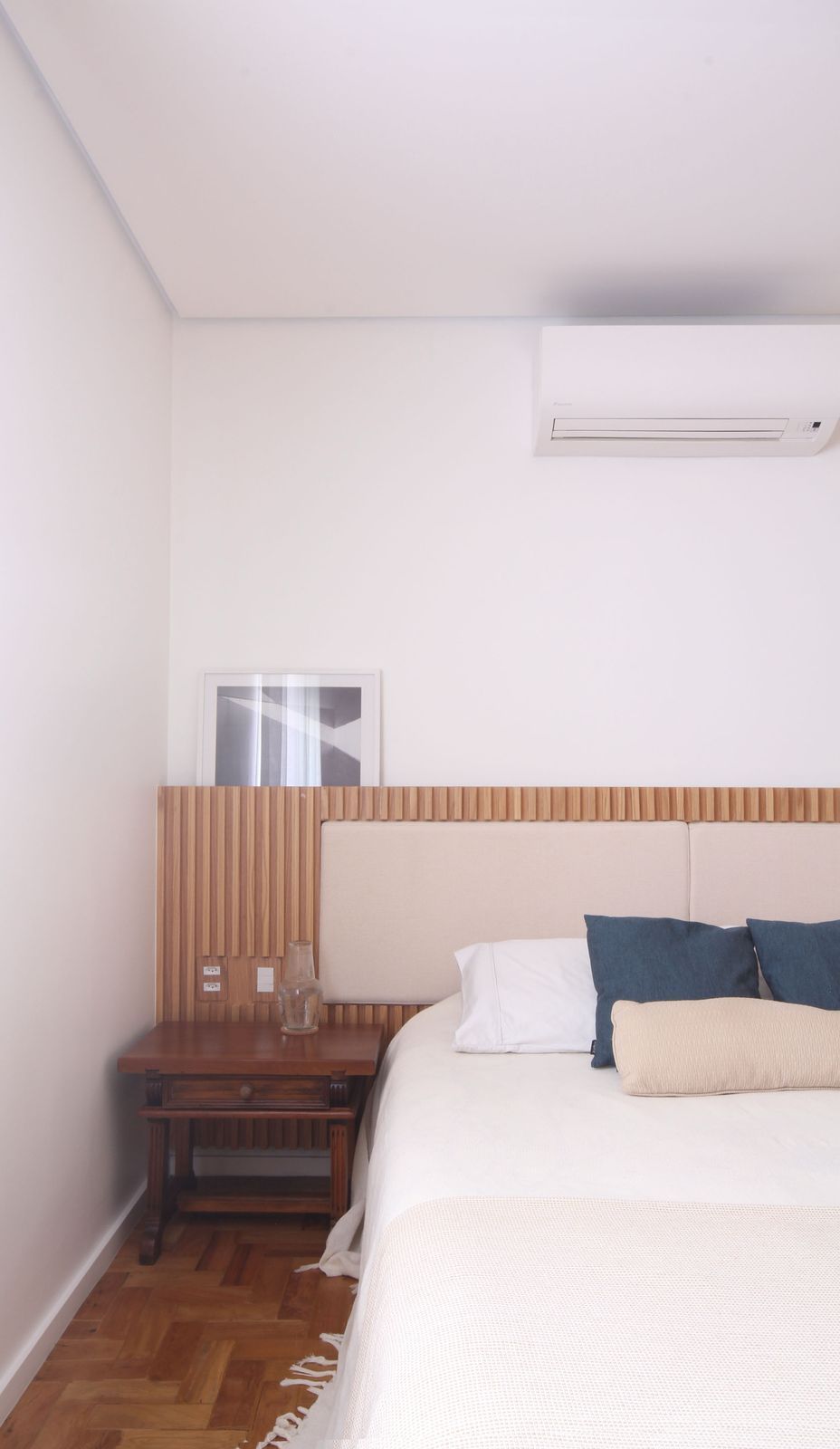 Quarto minimalista com cama, mesa de cabeceira, cabeceira de madeira e ar condicionado de parede.