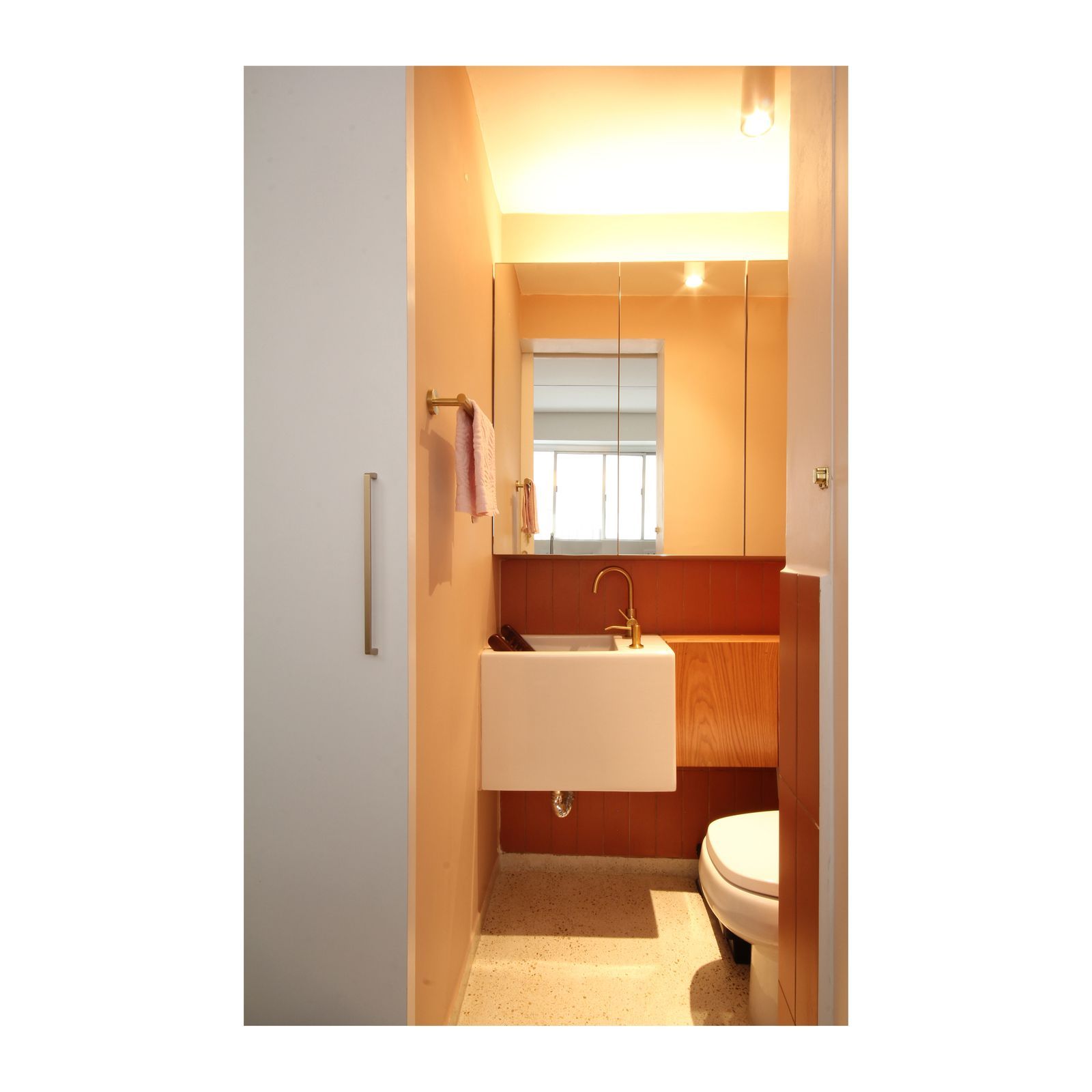 Banheiro compacto com pia suspensa, espelho, iluminação aconchegante e vaso sanitário no canto.