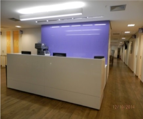 Recepção de escritório vazia com mesa branca, parede com detalhes em roxo e corredor ao fundo.