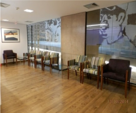 Sala de espera vazia com cadeiras, piso de madeira e obras de arte em vidro fosco na parede.