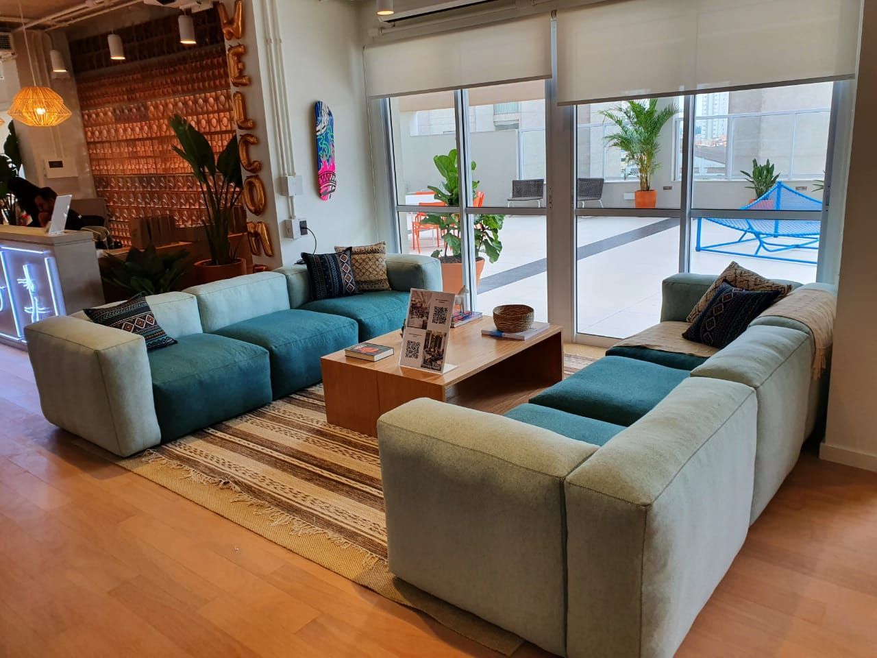 Sala de estar moderna com sofás modulares azul-petróleo, mesa de centro de madeira, tapete e portas de vidro que dão para um pátio com piscina.