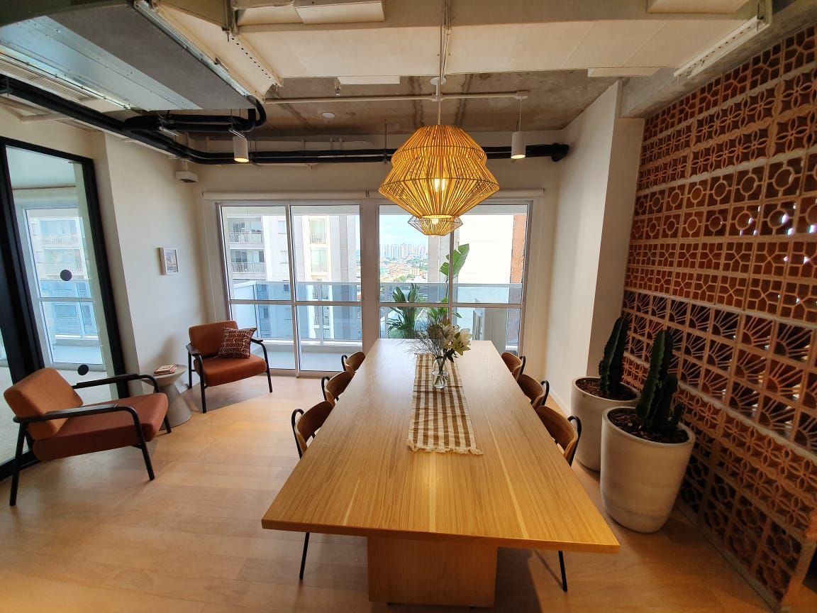 Sala de jantar moderna com mesa comprida de madeira, luminária pendente de vime e vista para a varanda.