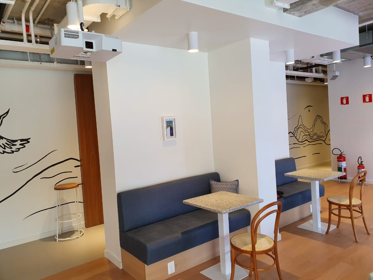 Área de estar moderna com bancos azuis, mesinhas e paredes de vidro fosco em um interior luminoso.