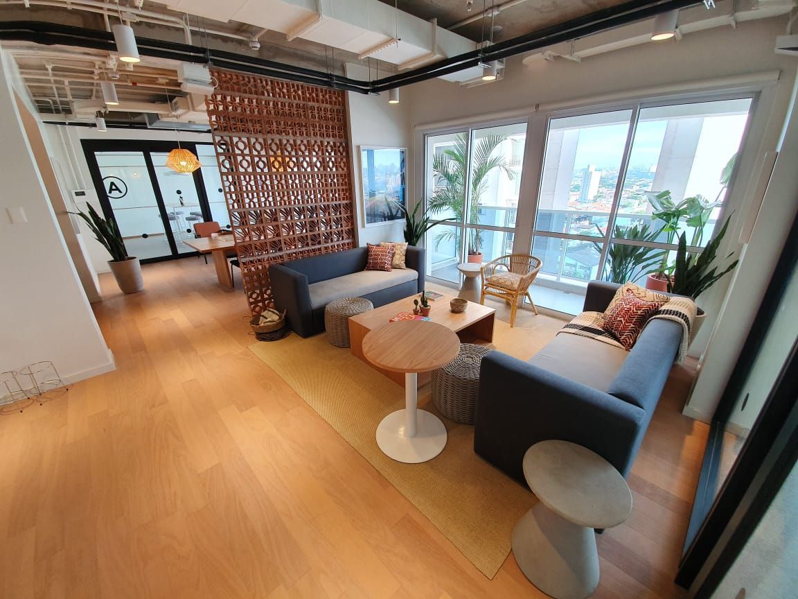 Sala de estar moderna com sofás azuis, piso de madeira, mesas redondas e grandes janelas com vista para a vegetação.