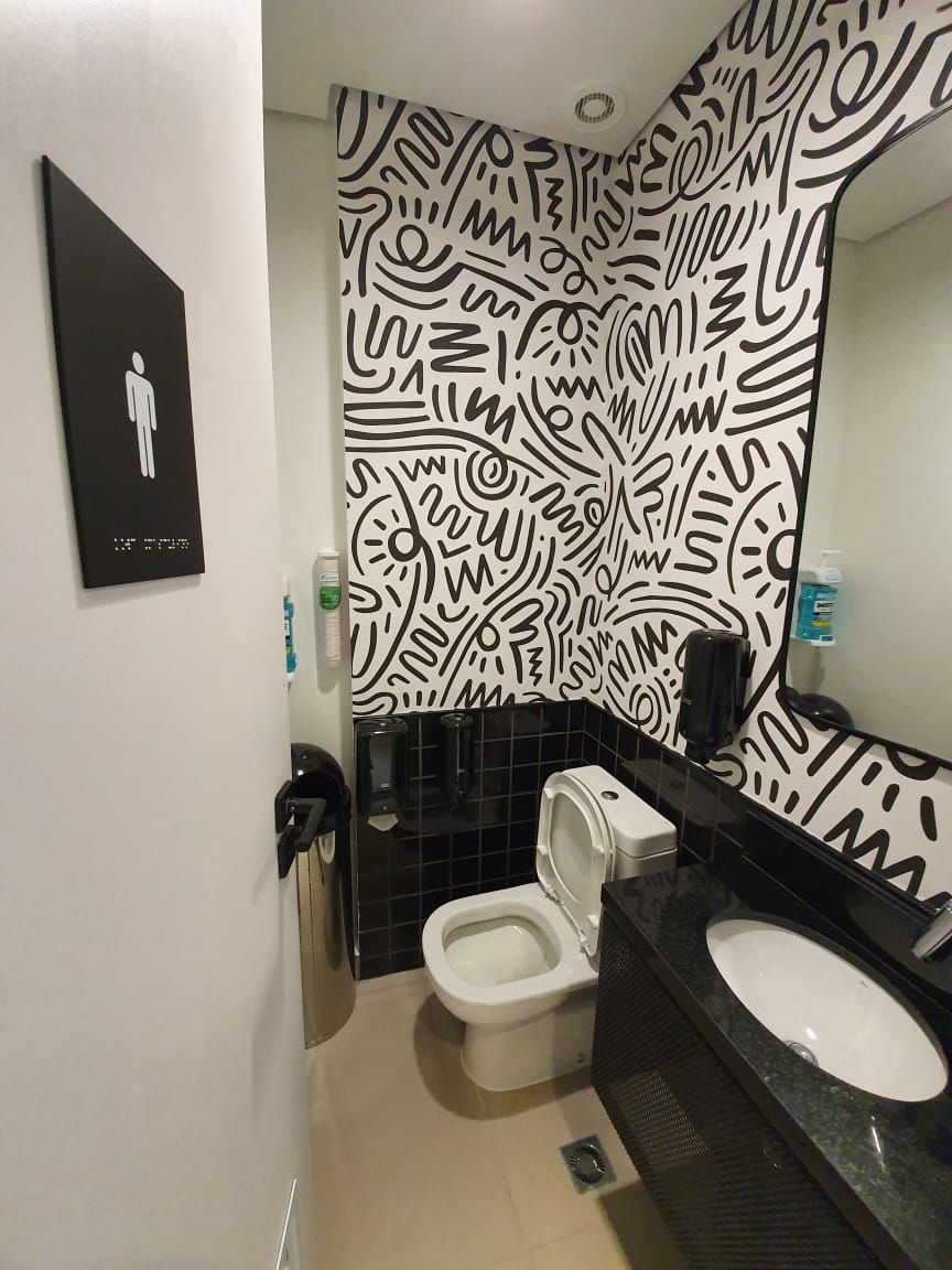Pequeno banheiro com paredes estampadas em preto e branco, vaso sanitário, pia e placa indicando que é um banheiro feminino.