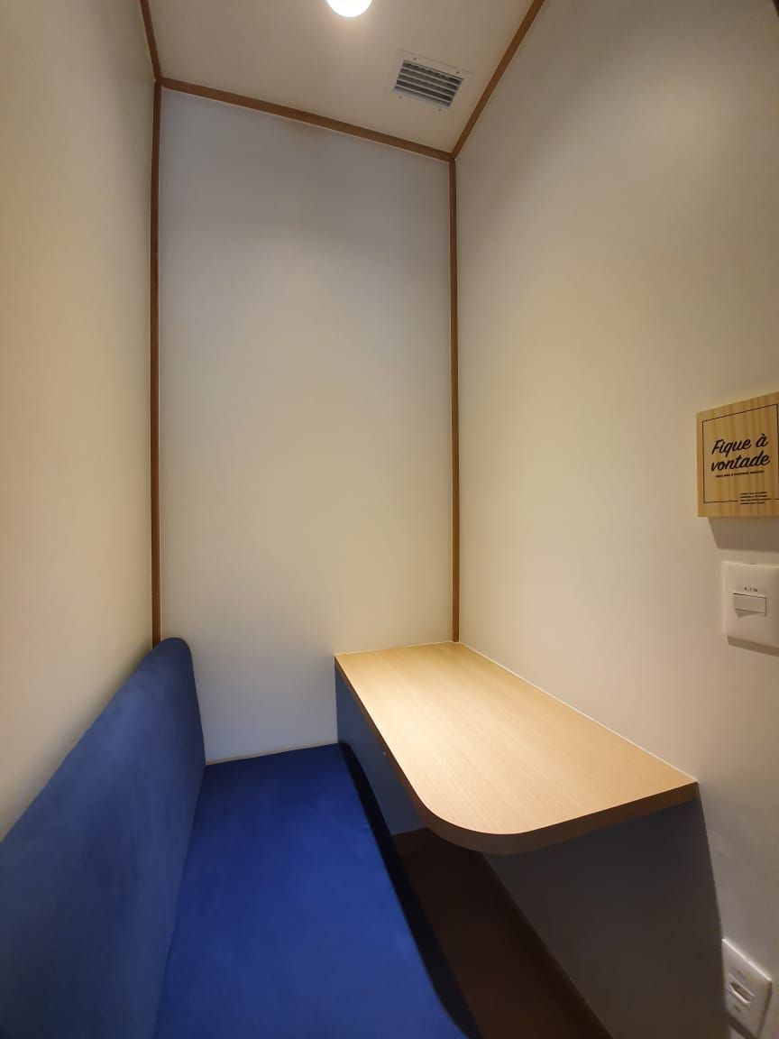 Pequena cabine privativa com banco azul e mesa de madeira clara sob iluminação interna suave.