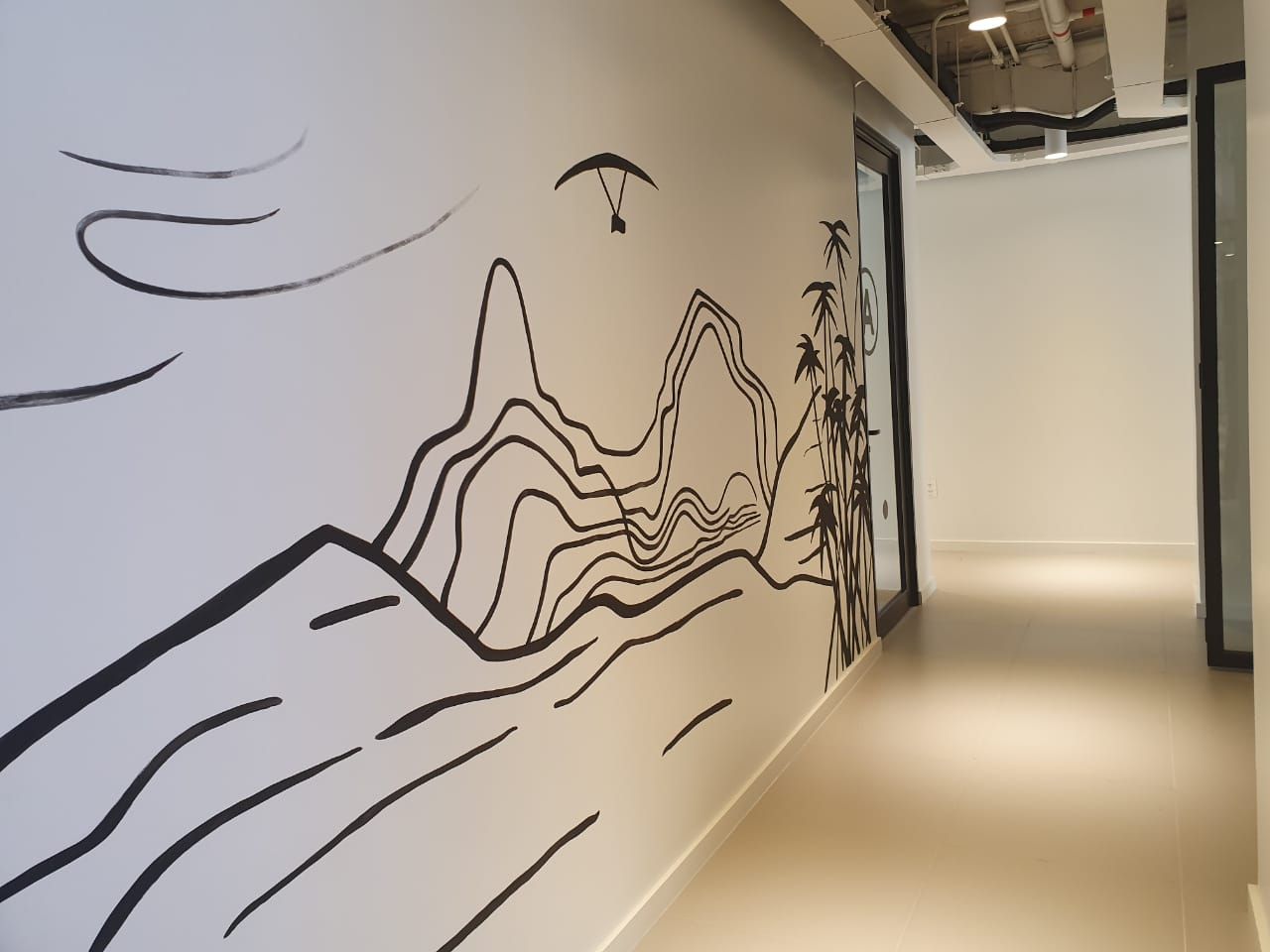 Mural em preto e branco com desenhos de montanhas e árvores ao longo de uma parede de corredor.
