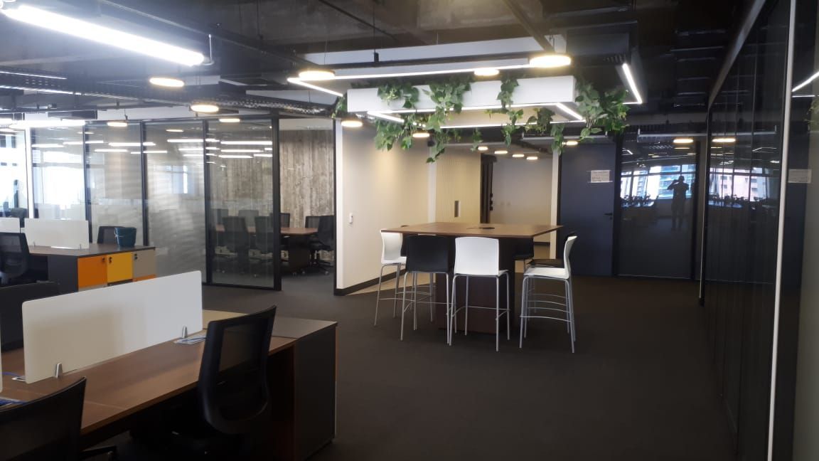Espaço de trabalho moderno com salas envidraçadas, mesas, cadeiras e uma mesa de reuniões redonda.