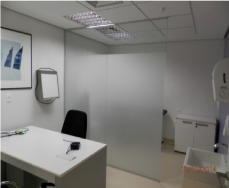 Escritório branco vazio com mesa, cadeira, obras de arte na parede e divisórias de vidro fosco.