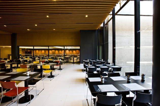 Sala de jantar moderna de restaurante com mesas pretas, cadeiras laranja e janelas amplas.